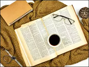 Filiżanka kawy i okulary na książce obok notesu na swetrze