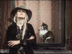 Dziewczyna w kapeluszu i kotek widoczny w oknie