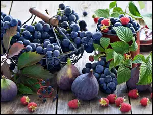 Kiście winogron w koszyczku obok fig i malin na deskach
