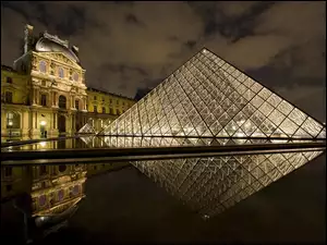 Muzeum Luwr w Paryżu nocą i odbicie w wodzie