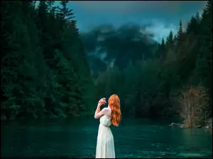 Rudowłosa kobieta nad rzeką otoczoną lasem