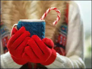 Dłonie w czerwonych rękawiczkach trzymają kubek z napojem