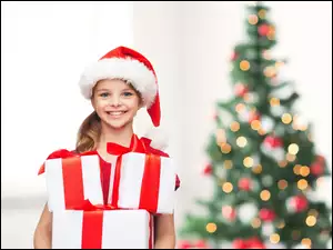 Dziewczynka w czapce mikołaja ze świątecznymi prezentami