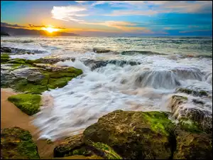 Zachód słońca nad morzem i fale rozpryskujące się o kamienie