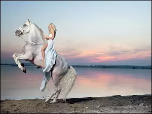 Kobieta na białym koniu nad jeziorem