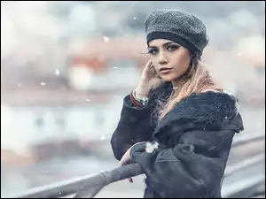 Blondynka w zimowej czapce z makijażem na moście oparta o barierkę na rozmytym tle