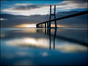 Most odbija się w morzu o wschodzie słońca