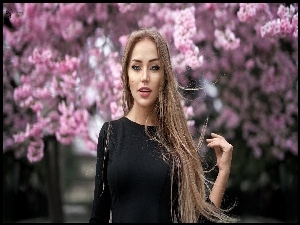 Kobieta z długimi włosami na tle kwitnącego drzewa owocowego