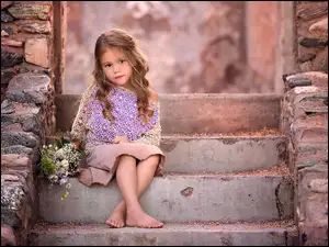 Dziewczynka z bukietem kwiatów siedzi na betonowych schodach
