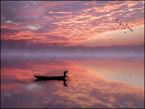 Łódka chmury i lecące ptaki odbijają się w zamglonym jeziorze