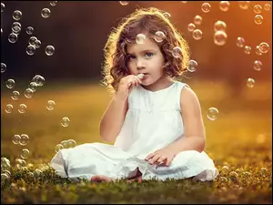 Bańki mydlane fruwają wokół dziewczynki siedzącej na trawie