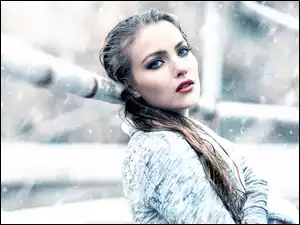 Kobieta oparta o ogrodzenie w padającym śniegu