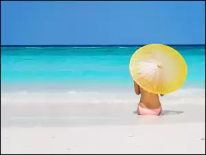 Kobieta w stroju kąpielowym z parasolką siedzi na morskiej plaży