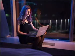 Dziewczyna z laptopem na kolanach siedzi przy oknie