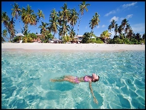 Dziewczyna pływająca w morzu z widokiem na plażę z palmami