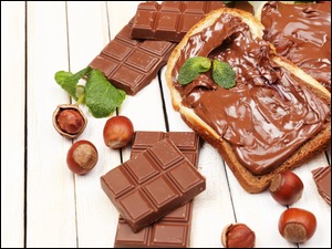 Kanapki posmarowane czekoladą obok orzechów i tabliczek czekolady