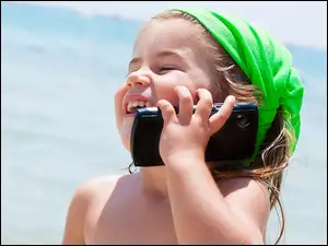 Uśmiechnięta dziewczynka z telefonem nad morzem