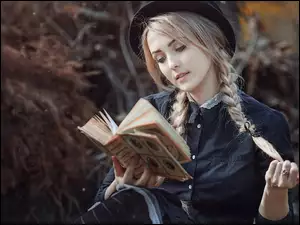 Blondynka w kapeluszu z warkoczami czyta książkę