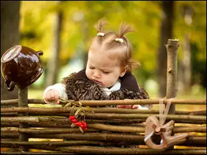 Mała dziewczynka z kucykami obok drewnianego ogrodzenia z gałązką jarzębiny w rączce
