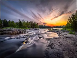 Rzeka płynąca między skałami i drzewami o zachodzie słońca
