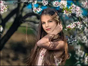Dziewczynka pozuje do zdjęcia pośród gałązek drzewa owocowego