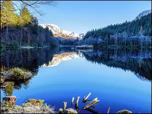 Malowniczy krajobraz na jezioro pod lasem u podnóża gór z ośnieżonymi szczytami