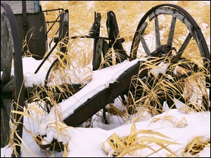 Zniszczona stara maszyna rolnicza w trawie zasypanej śniegiem