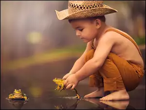 Chłopczyk w kapeluszu puszcza żaby do wody