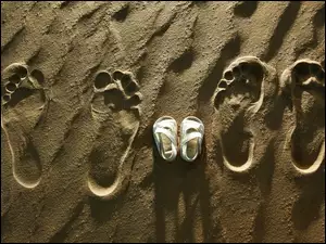 Dziecięce sandałki pomiędzy śladami stóp na piasku