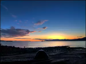 Namiot na brzegu jeziora z widokiem na zachodzące słońce