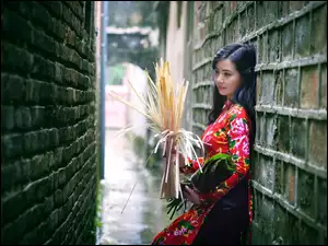 Kobieta z bukietami liści i trawy stoi oparta o mur