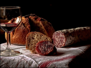 Chleb i kiełbasa położona na ściereczce obok kieliszka z winem