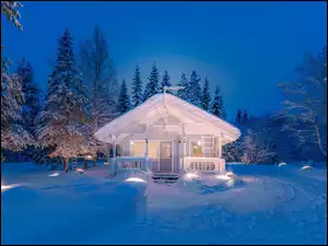 Oświetlony domek w zaśnieżonym lesie nocą