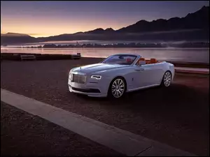 Rolls- Royce Dawn z roku 2016 stoi na placu obok rzeki o zachodzie słońca