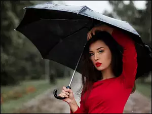 Kobieta chroni sie pod parasolem przed deszczem
