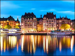 Statki i oświetlone domy odbijają się w sztokholmskiej rzece