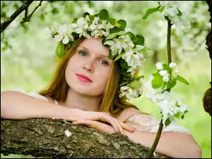 Kobieta w wianku z kwitnącej gałązki przy drzewie