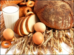 Chleb i jajka położone na kłosach zboża obok szklanki z mlekiem