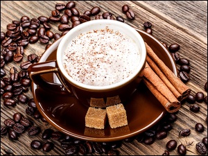 Filiżanka z kawą postawiona na drewnianym blacie z rozsypanymi ziarnami kawy