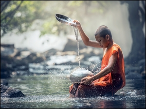 Młody mnich w rzece polewa wodą naczynie