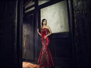 Azjatka w czerwonej sukience stoi przy ścianie