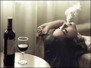 Butelka z winem i kieliszek oraz kobieta paląca papierosa