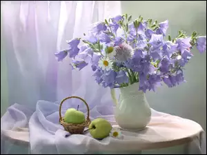 Kompozycja z kwiatów rumianku i dzwonków obok zielonych jabłek na stoliczku