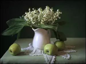 Kompozycja z bukietu konwalii majowej w dzbanku i jabłkami obok na stole
