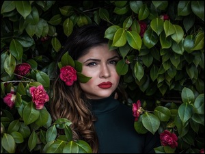 Kobieta pozuje pośród liści i czerwonych kwiatów