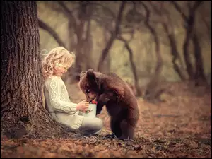 Dziewczyna karmi niedźwiadka owocami z garnuszka