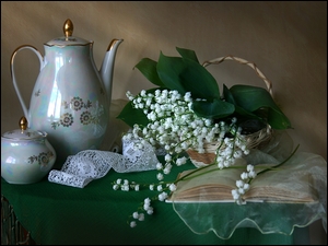 Kompozycja z konwalii majowej w koszyku obok książki i zestawu do herbaty
