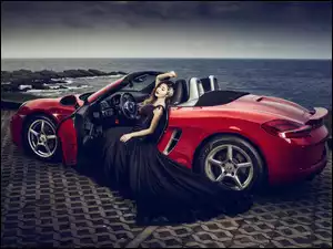Kobieta w długiej sukni w czerwonym Porsche Cabrio
