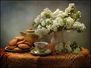 Naleśniki na talerzu obok filiżanki z herbatą i bukietu kwiatów w wazonie