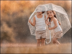 Dzieci pod parasolem w padającym deszczu